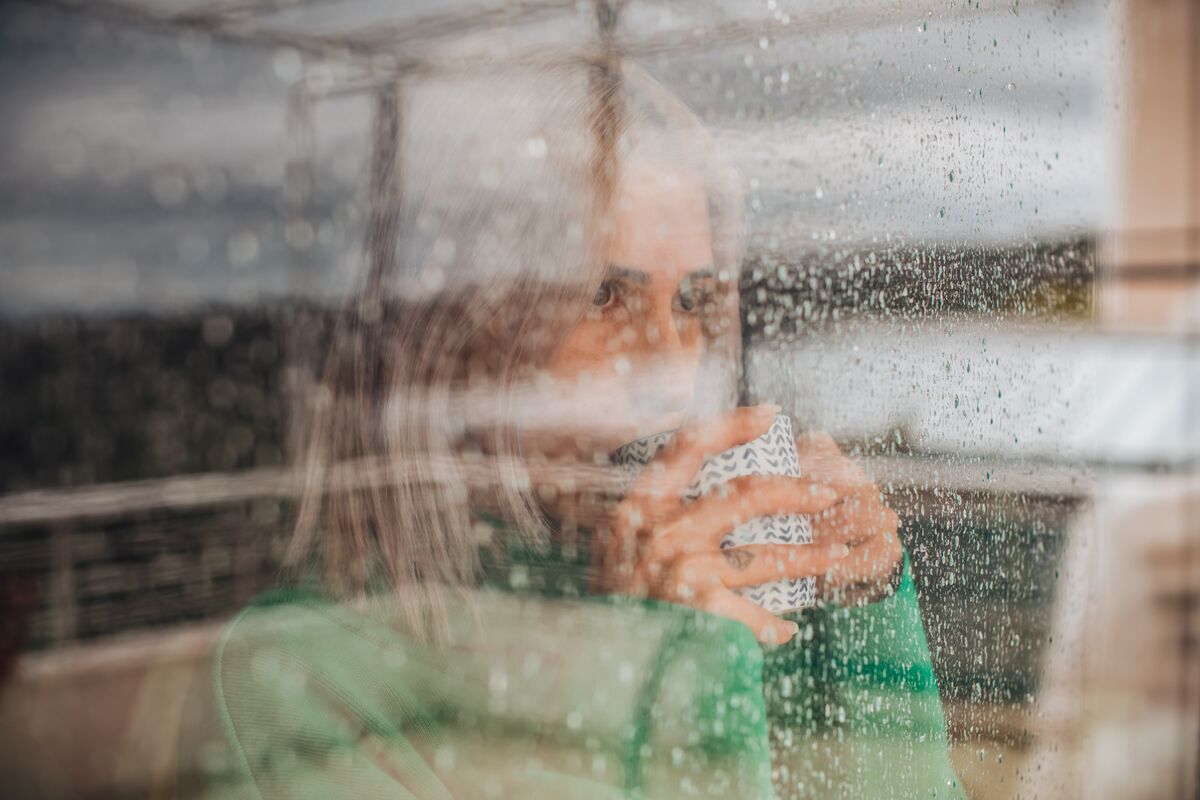 Woman drinking coffee behind glass window on a rainy day.